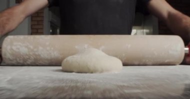 İsimsiz bir adamın mutfakta pizza hazırlarken masaya taze hamur germek için merdane kullanmasına odaklan.