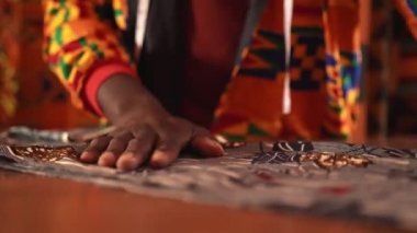 Turuncu ceketli Afro-Amerikan terzi gündüzleri dikiş atölyesinde çalışırken mavi tekstili makasla kesiyor.