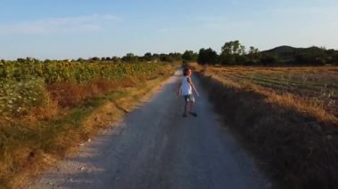 Güneşli bir günde kırsal bölgedeki ayçiçeği tarlasının yakınındaki kumlu yolda koşan genç bir çocuğun Drone görüntüsü.