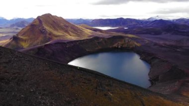 İzlanda 'nın dağlık bölgelerinde bulutlu bir günde tepenin arkasındaki sakin volkanik göl manzarası nefes kesici.