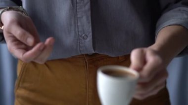 Yakından bakınca, evde dinlenirken bir fincan taze demlenmiş aromatik espresso alan kimliği belirsiz bir kadın görülüyor.