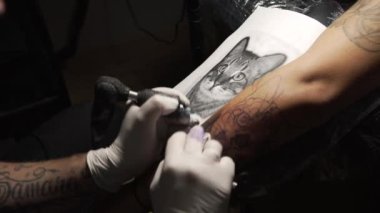Makina kullanan ve kuaförde siyah mürekkeple dövme yapan yüzsüz bir dövmeci.