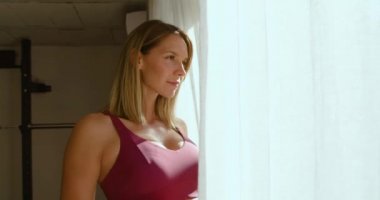 Eğitimden sonra evde panoramik pencereden dışarı bakarken şişeden su içen zayıf kadının yan görüntüsü