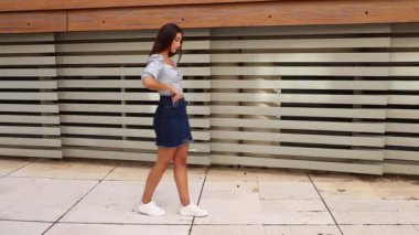 Modern binanın kepenkli penceresinin yanında yürürken konuşan şık bluzlu, genç bir etnik kadın.