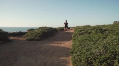 Siyah aktif giysili kadın huzurlu günbatımında yeşil deniz kenarında koşuyor.