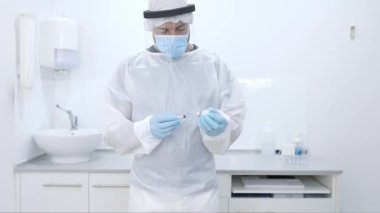 Ekin, modern donanımlı hastanede çalışırken cerrah önlüğü eldivenleri ve yüz kalkanı ile şırıngayı şişeden aldığı ilaçlarla dolduran profesyonel erkek tıp doktoru.