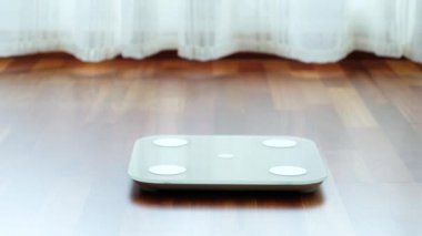 Üstten görünüşlü, çıplak ayaklı, rahat pijamalı, dijital ağırlığı ve vücut yağı terazisi üzerinde duran ve sabah banyoda 60 kg ağırlığında sağlıklı ağırlığı gösteren çıplak ayaklı bir kadın.