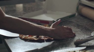 Kürekle tanınmayan erkek pizzacılar pizzacıda çalışırken taze pişmiş lezzetli dilimlenmiş pizzaları karton kutuya koyarlar.