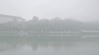 Dalgalanan nehir suyu, yamaçtan geçen bir gemi, yeşil ağaçlar ve kırsal alanda, sisli havada kır evi olan bir köy.