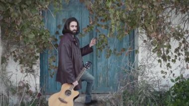 Gitarla dikilen müzisyen başka tarafa bakıyor.