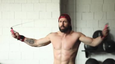 Ağır çekimde beden eğitimi sırasında kaslı üstsüz erkek atlet ip atlıyor.