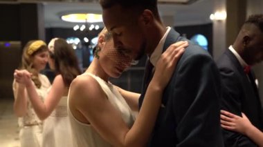 Zarif gelin ve şık Afro-Amerikan damadın düğün günü misafirlerle dans edişinin yan görüntüsü.