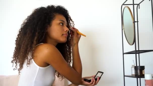 在家庭日常化妆过程中 年轻卷曲头发的女性在镜子前用化妆品刷从面颊上的调色板上涂上腮红的侧视图 — 图库视频影像
