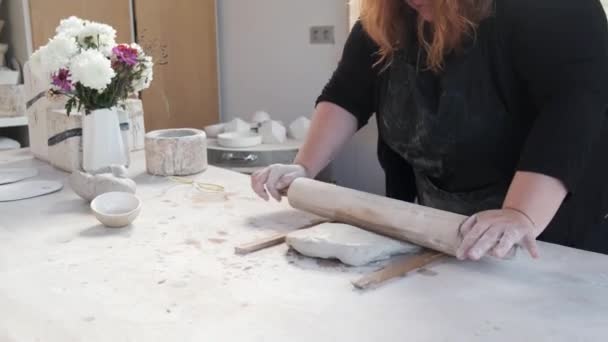 Ernte unkenntliche Kunsthandwerkerin in Schürze mit Nudelholz und Holzstäben bei der Herstellung von Ton für die Bildhauerei