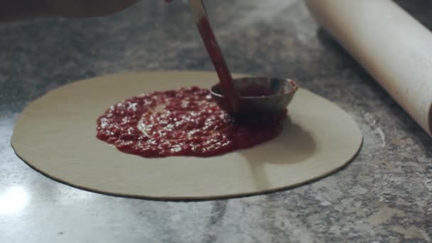 在餐馆厨房里 用勺子把番茄酱倒在面团上 同时在有各种配料的大理石桌上做披萨 — 图库视频影像