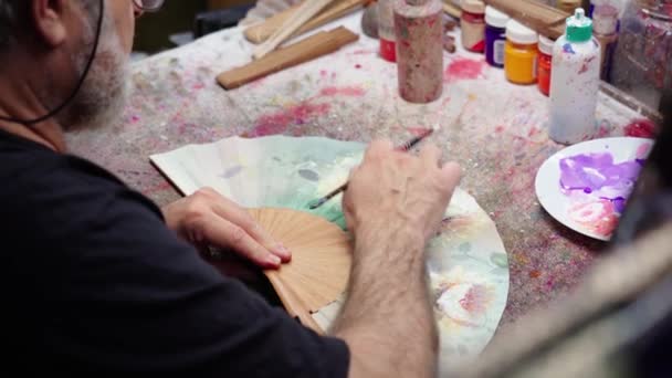 Ζωγράφος Χρησιμοποιώντας Πινέλο Για Σχεδιάσετε Στο Χέρι Ανεμιστήρα Ενώ Κάθεται — Αρχείο Βίντεο
