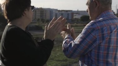 Güneşli bir günde banliyöde dikilip el çırpan ve gülümseyen yaşlı çiftlerin gerçek zamanlı videosu.