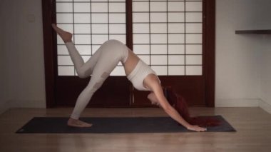 Genç kızıl saçlı kadın evde yoga yapıyor.