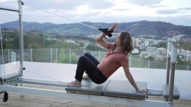 Urdhva Dhanurasana 'da pilates makinesinde kayışları olan ve terasta yoga yaparken vücudunu esneten esnek erkeğin yan görüntüsü