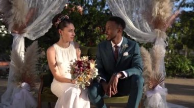 Neşeli gelin ve damat düğün günü süslü kemerlerin altında oturuyor.