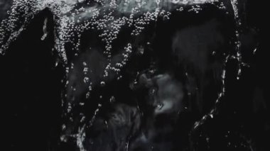 Şeffaf suyun aktığı ve siyah arkaplana karşı yavaş çekimde sıçrayan soyut arkaplan