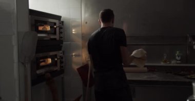 Lokanta mutfağındaki pizza tabanını gererken unlu hamur atan isimsiz bir adamın arka plan görüntüsü.