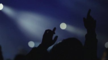 Müzikal performans sırasında siyah ışık sahnesiyle aydınlanmış elleri havada insanların arka plan siluetleri