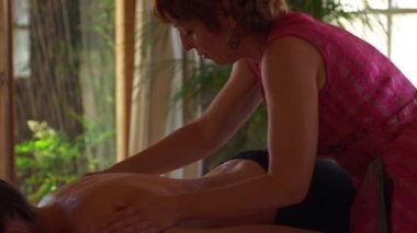 Modern salonda rahatlamış müşterinin sırtında aromatik yağ ile ayurvedik masaj yaparken yan görünüm