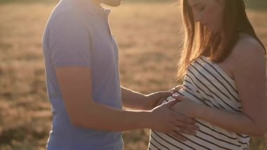 Gün batımında kuru tarlada dururken hamile bir kadının karnına nazikçe dokunan tanınmayan bir adamın yan görüntüsü.