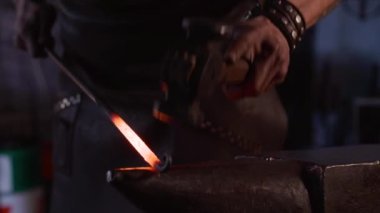 Geleneksel demircilikte çalışırken genç ve vahşi zanaatkârın apron ısıtma ve örse çekiçle vuruşunun yan görüntüsü