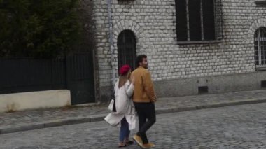 Sonbahar günü Paris 'in eski sokaklarını keşfederken, taş bina yakınlarında yürürken, sıcak giysiler içinde neşeli romantik bir çiftin çekimleri.