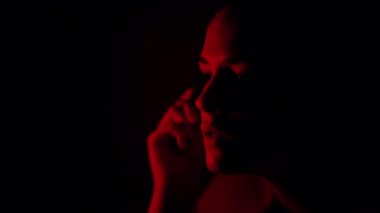 Sakin bir kadın siyah arka planda kırmızı ışıkla karanlık stüdyoda makyaj yaparken kirpik makyajı yapıyor.