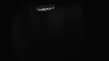 Kapalı metal madeni para, siyah arka plandaki karanlık odada ağır çekimde kaburga üzerinde dönüyor.