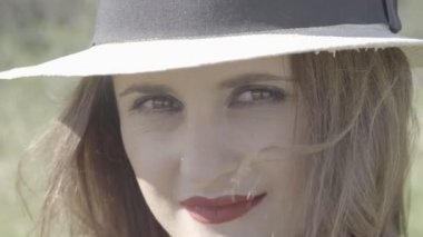 Güneşli bir günde kameraya bakan şapkalı neşeli bir kadın.