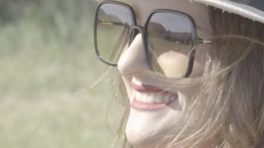 Güneşli bir günde kameraya bakan şapkalı neşeli bir kadın.