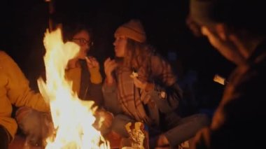 Group of tourists frying marshmallows in bonfire