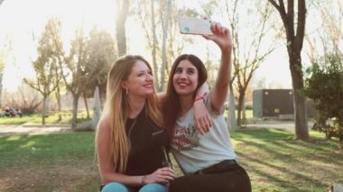 Gülümseyen kadınlar parkta selfie çekiyorlar.