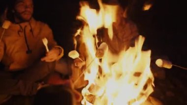 Group of tourists frying marshmallows in bonfire