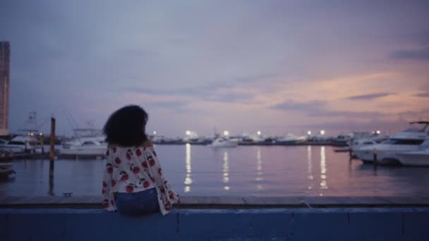 妇女坐在靠近水和游艇的堤岸上 — 图库视频影像