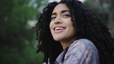 Siyah kadın doğada duruyor ve kameraya bakıyor.