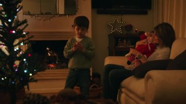 Anne bebekle oynarken, oğul Noel ağacı süslüyordu.