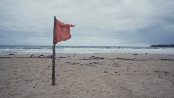 在空旷的沙滩上挂着摇曳着红布的木棍 背景是汹涌的海浪 — 图库视频影像