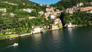 İtalya 'nın Dolomitler kentindeki Como Gölü' nün köpüklü sularının yanındaki yemyeşil yamaçlar boyunca uzanan büyüleyici köy binalarının havadan görünüşü berrak mavi bir gökyüzünün altında..