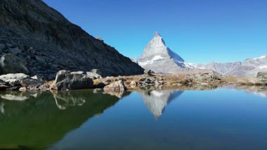 Matterhorn 'un berrak mavi gökyüzünün altındaki engebeli dağ manzarasıyla çevrili sakin bir alp gölüne yansıyan nefes kesici manzarası doğanın sükunetini yansıtıyor..