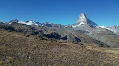 İkonik Matterhorn, engebeli kayalıklarla çevrili açık mavi bir gökyüzüne karşı dimdik ayakta duruyor. Görkemli dağ İsviçre Alpleri ve doğal güzelliğin bir sembolüdür..