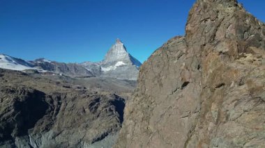 Matterhorn, engebeli, kayalık arazi tarafından çerçevelenmiş karlı zirvesi olan canlı mavi gökyüzünün altında gururla duruyor. Muhteşem dağ, İsviçre manzaralarının güzelliğini somutlaştırıyor..