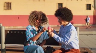 İki arkadaş, şehir merkezinde bir bankta oturup leziz dondurma külahlarının tadını çıkararak keyifli bir anı paylaşıyor. Sıcak atmosfer, canlı şehirdeki neşeli günlerine yeni bir hava katıyor..