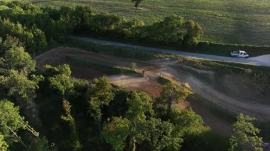 Motokros sürücülerinin verimli yeşilliklerle çevrili zorlu bir toprak yolda yol almalarının heyecanını ve heyecanını gösteren hava manzarası..