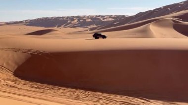 Tek bir araç, Libya 'nın Erg Murzuk kentindeki geniş kum tepelerini aşarak açık bir gökyüzü altında ilerliyor. Uçsuz bucaksız altın manzara çöl macerasının özünü temsil ediyor..