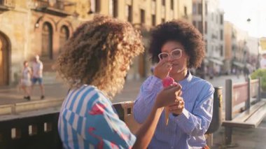 İki arkadaş şehir merkezinde güneşli bir günde dondurmanın tadını çıkarıyorlar. Neşeli atmosfer ve tarihi mimari neşeli anları için canlı bir şehir arkaplanı oluşturuyor..